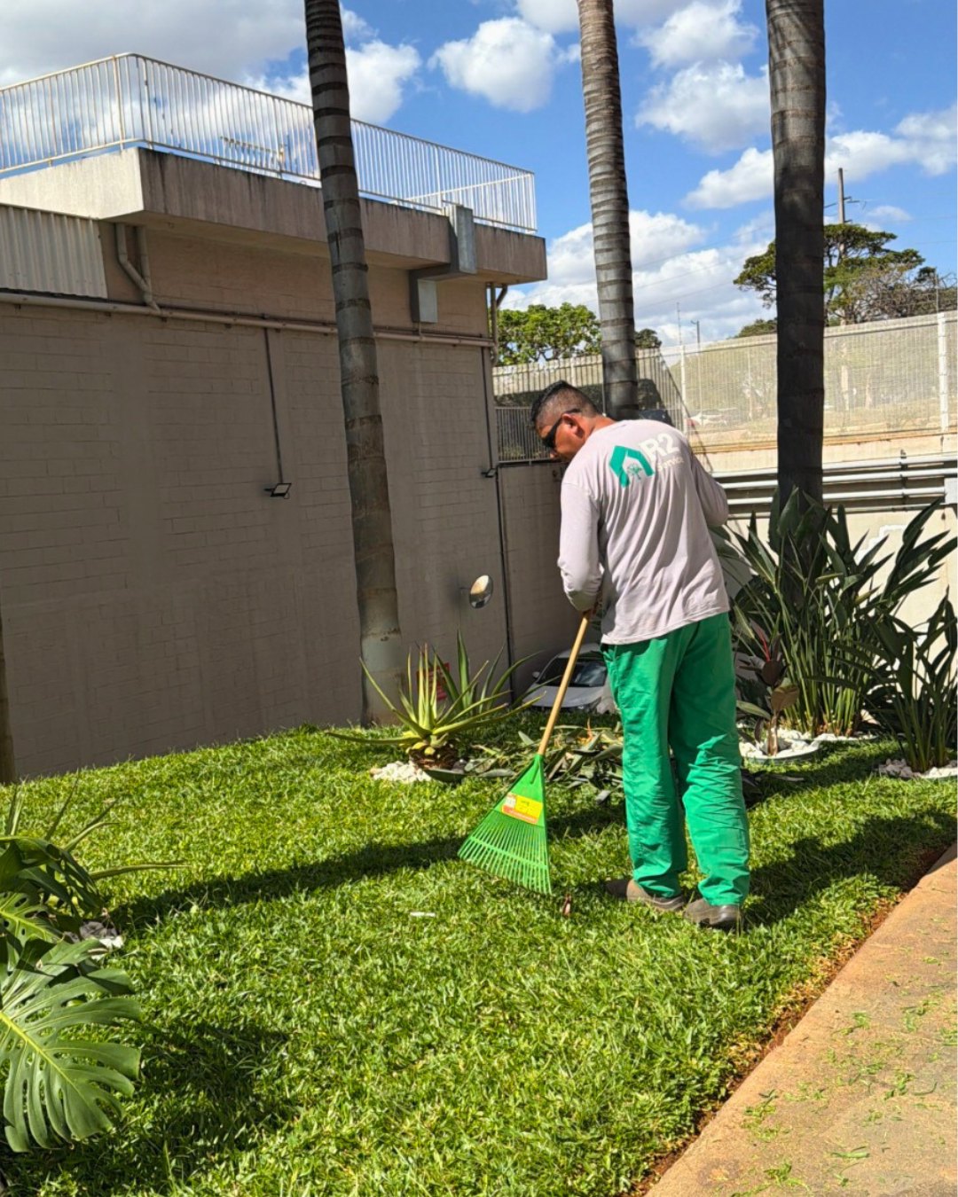 Profissional recolhendo resíduos com rastelo em área verde de edifício